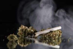 A lit marijuana joint resting on a couple cannabis buds.