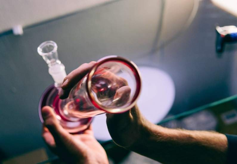 A person cleaning a glass beaker bong with alcohol and cotton swabs.